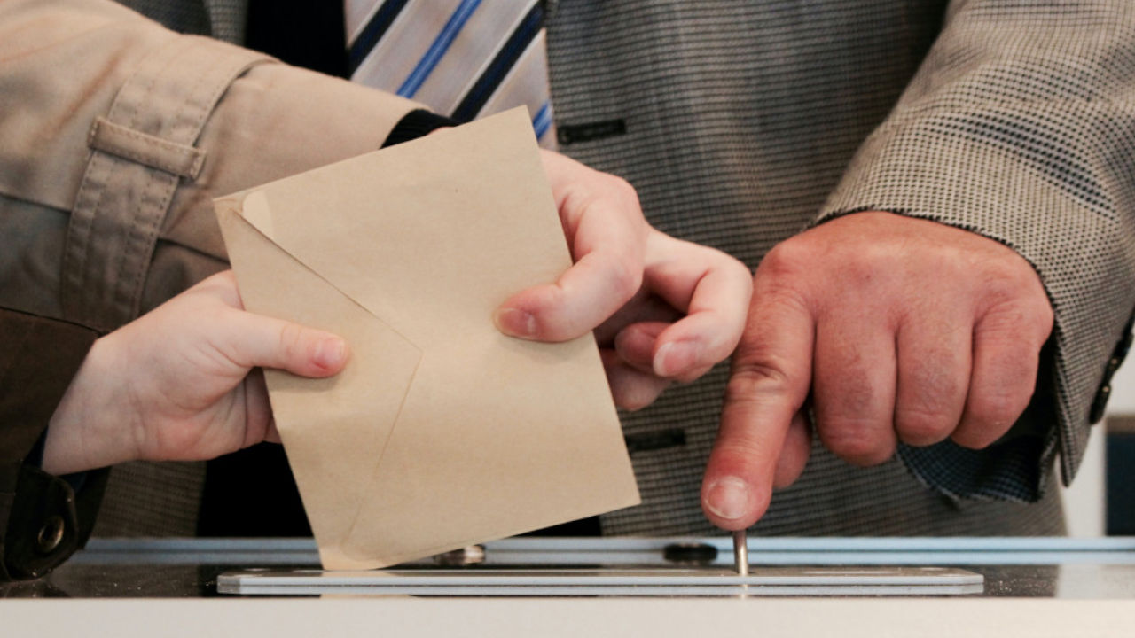Une personne déposant son bulletin de vote dans une urne.
